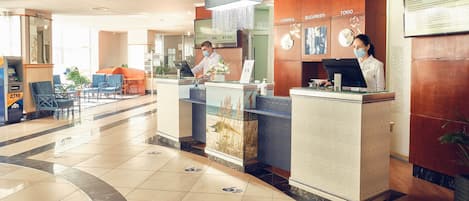 A hotel reception area with a modern design, featuring a reception desk, a digital clock, and a signboard with room names.