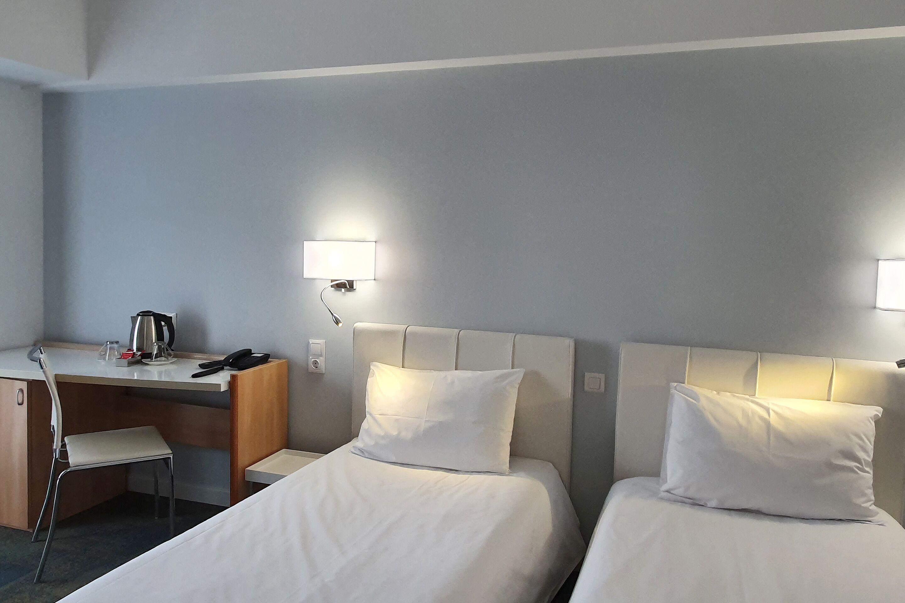 A hotel room with two beds, a desk, a chair, and a coffee maker.