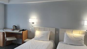 Habitación de hotel con dos camas, un escritorio, una silla y una cafetera.