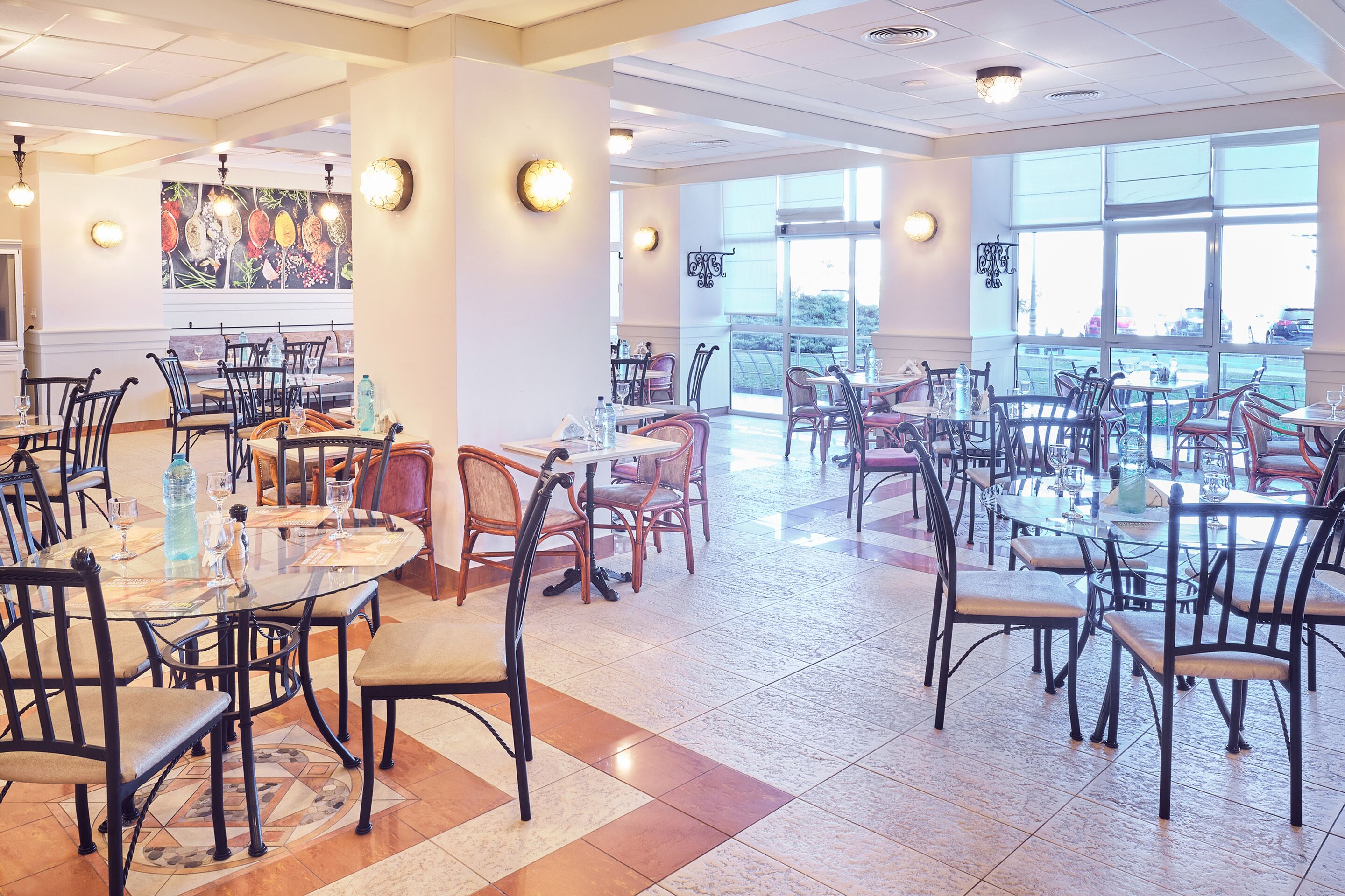 A spacious dining area with multiple tables and chairs, large windows providing natural light, and a decorative wall mural.