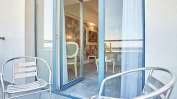 Un balcon avec deux chaises en métal, une porte vitrée donnant sur l’intérieur, et une vue sur l’espace intérieur, notamment un coin repas et un tableau accroché au mur.