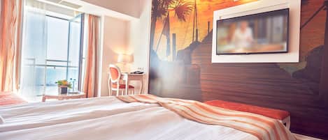 Habitación de hotel con cama, escritorio, silla, televisor y un amplio ventanal con cortinas.