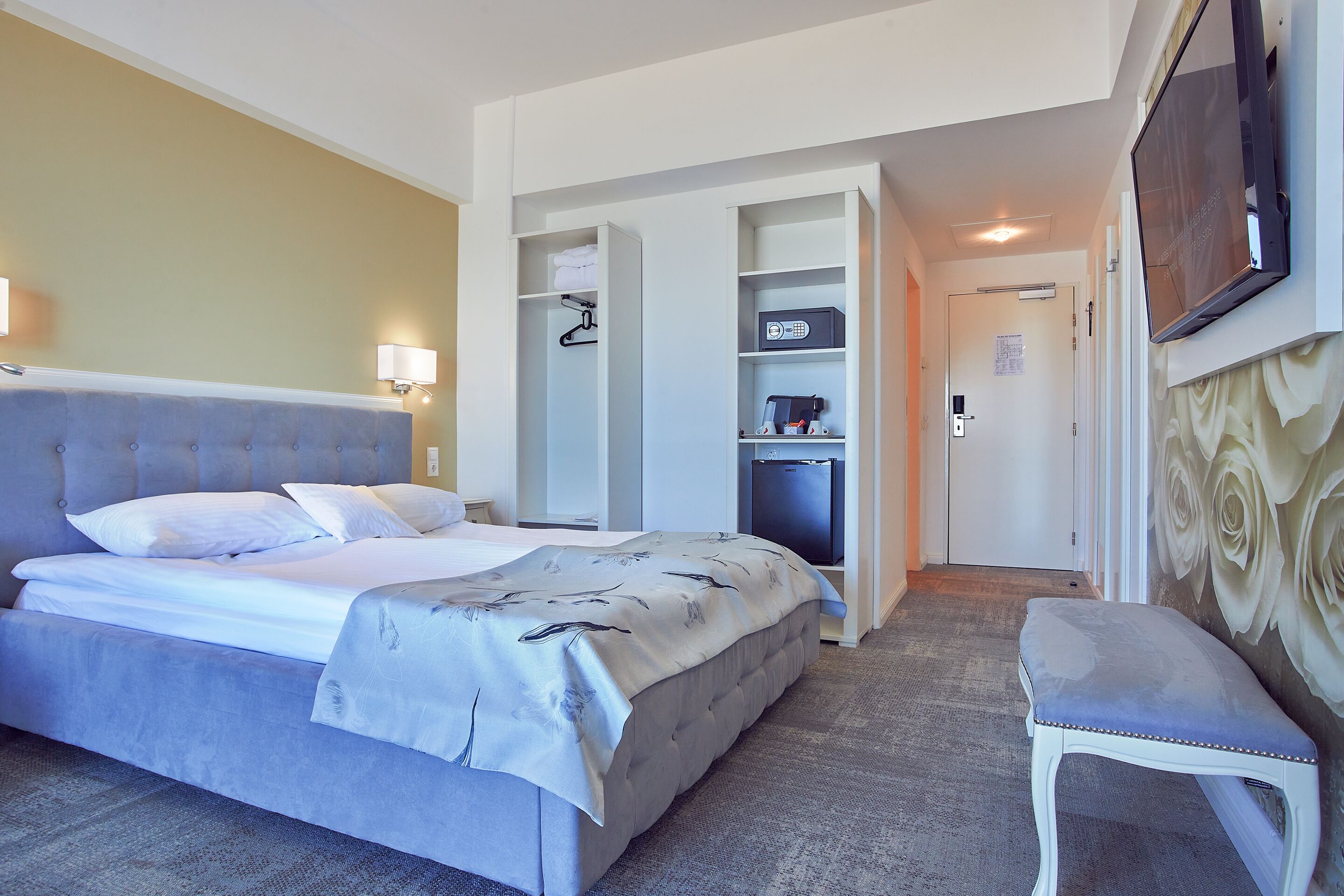 A hotel room with a bed, a bench, a wardrobe, and a television.