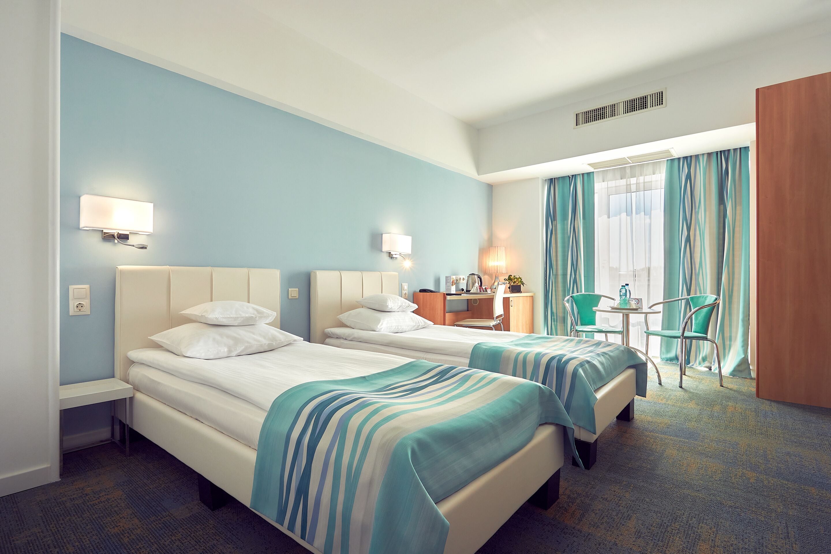 A hotel room with two beds, a desk, a chair, and a window with curtains.