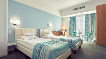 A hotel room with two beds, a desk, a chair, and a window with curtains.
