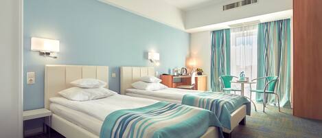 Habitación de hotel con dos camas, un escritorio, una silla y una ventana con cortinas.