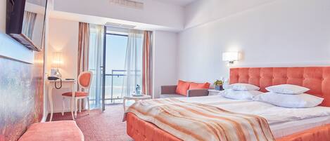 Habitación de hotel con una cama grande, un escritorio, una silla y un balcón con cortinas.