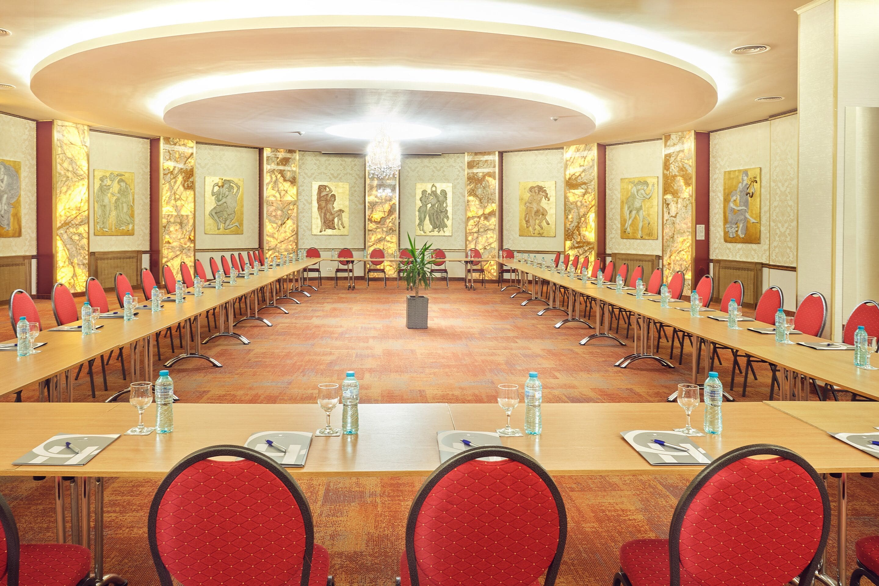 Une salle de conférence avec une longue table, des chaises rouges, des bouteilles d’eau et des verres.