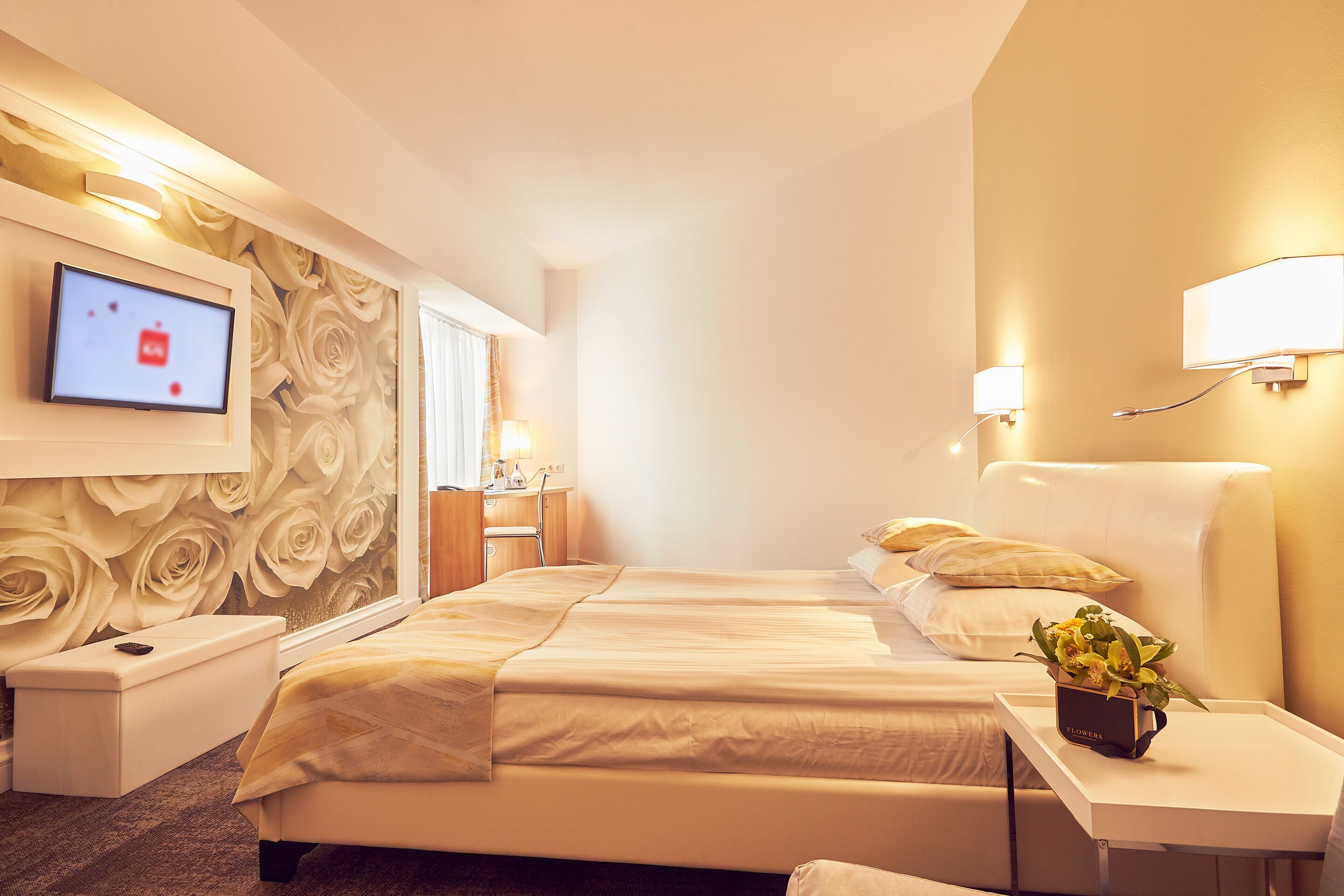A hotel room with a large bed, bedside tables, a TV, and a wall-mounted lamp.