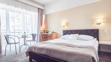 Una camera d'albergo con un letto grande, due comodini, una scrivania con una sedia e vista panoramica da ampie finestre.