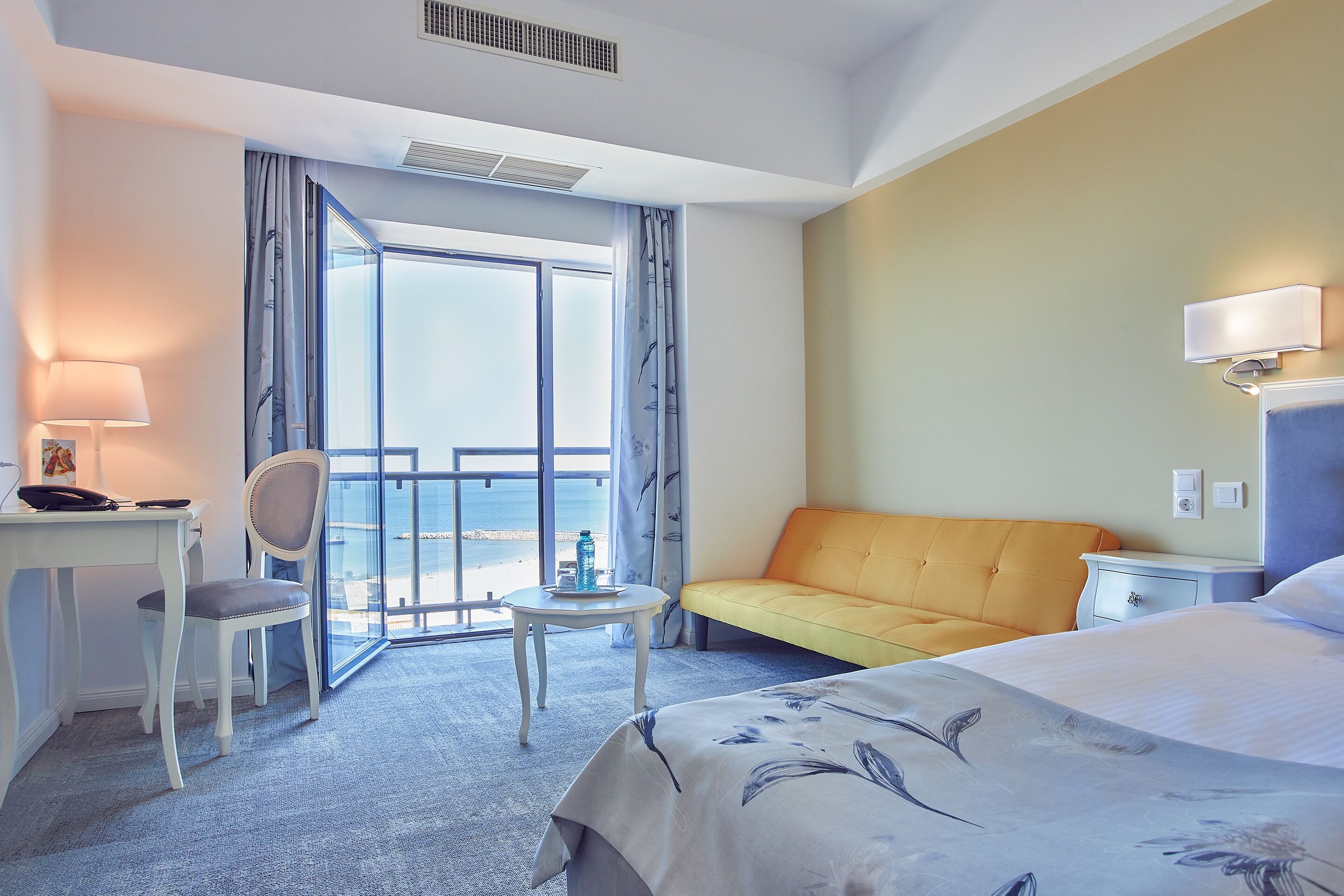A hotel room with a bed, a desk, a chair, a small table, and a sofa.