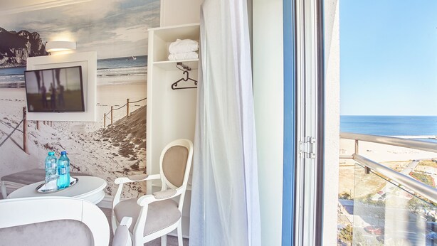 A hotel room with a balcony, a TV, a chair, a table with water bottles, and a shelf with towels. - Continental Forum Constanta (Constanta)