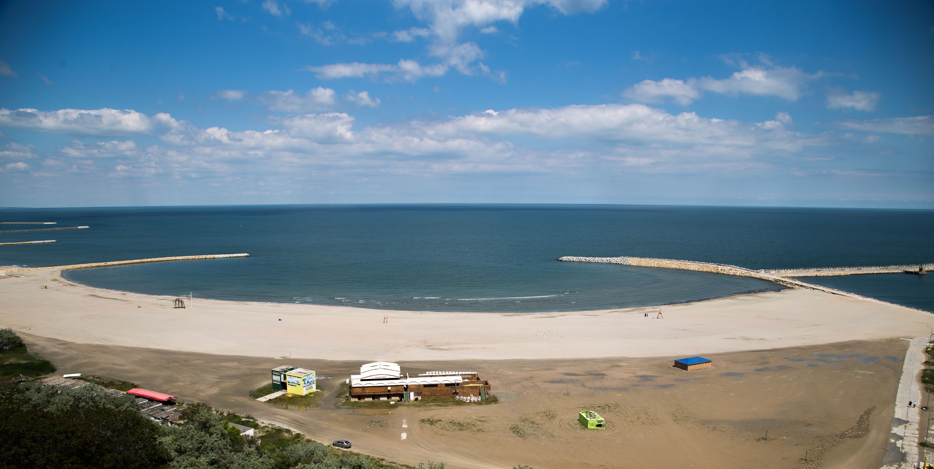 An aerial view of a beach with a large building, a sandy shore, and a clear blue sky.