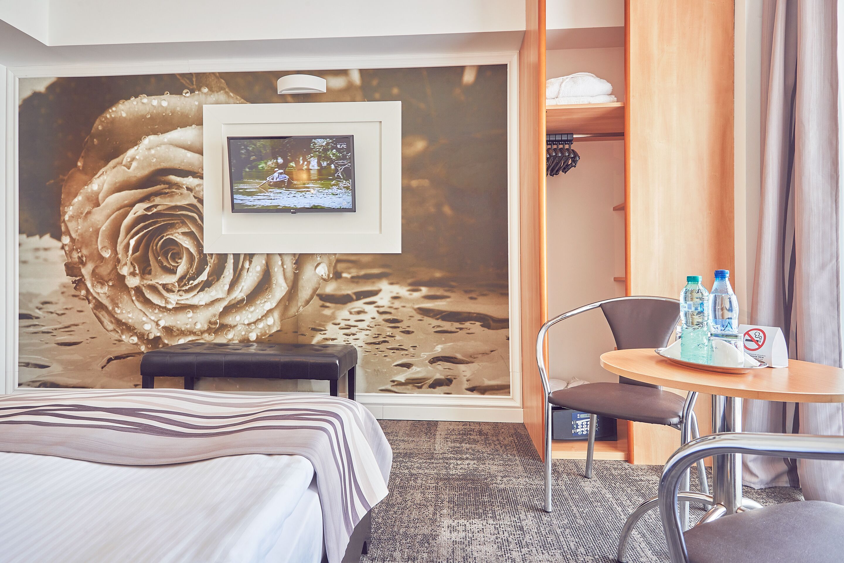 A hotel room with a bed, a desk with two bottles, a framed picture, and a large wall mural.