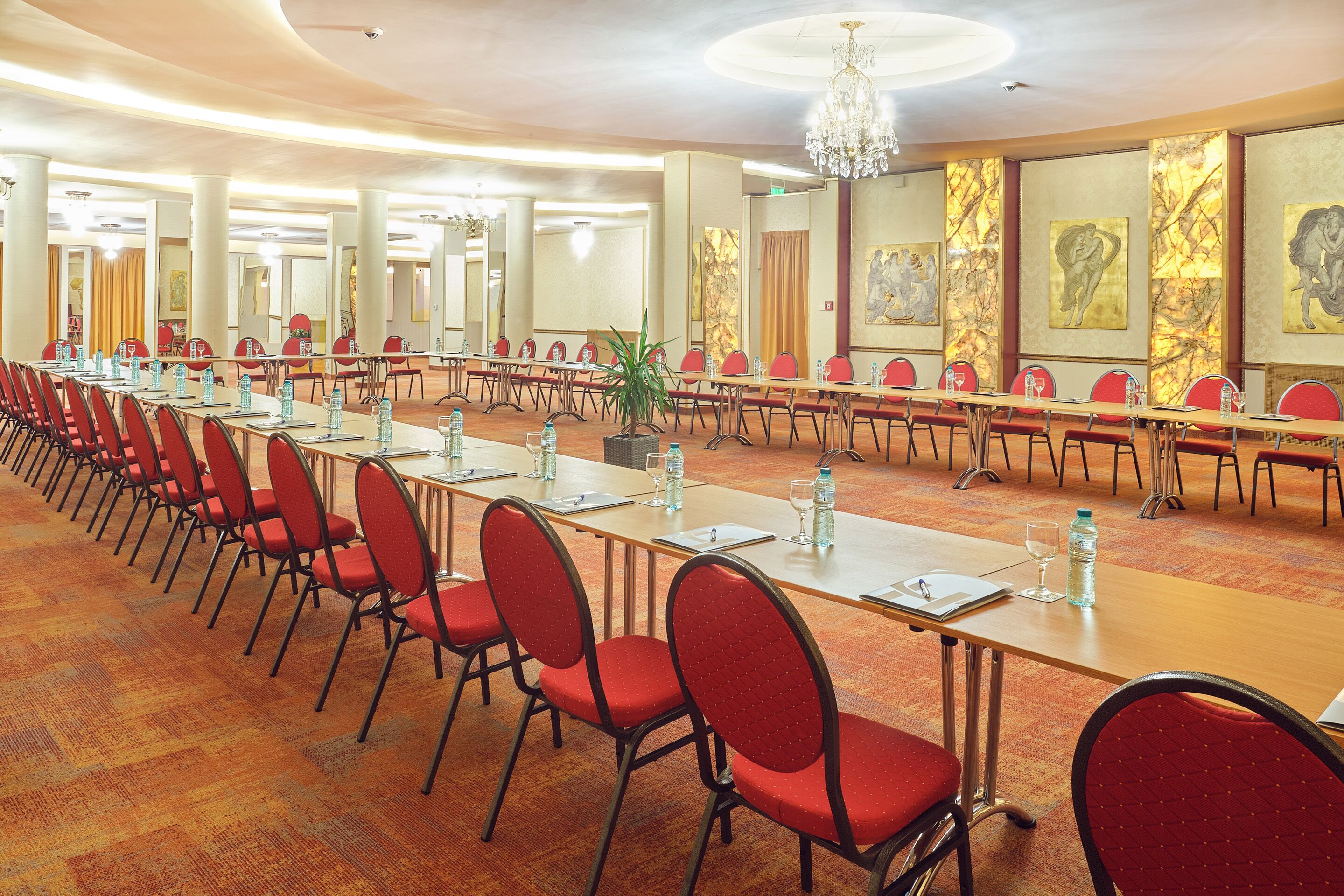 A conference room with long tables, red chairs, and water bottles.