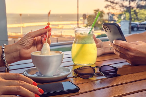 Una mesa de madera con una taza de café, un vaso de bebida fría, un teléfono inteligente y unas gafas de sol.