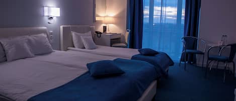 A hotel room with two beds, a desk, a chair, a nightstand, and a window with curtains.