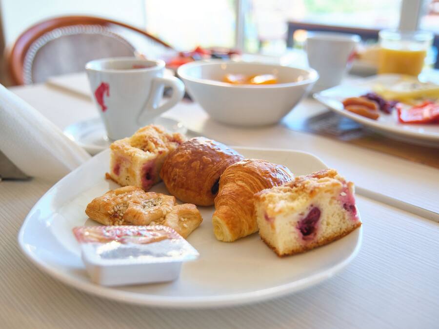 Un desayuno con bollos, un croissant y una taza de café sobre una mesa.