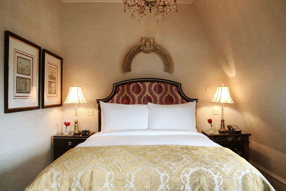 A neatly made bed with a patterned bedspread, two bedside lamps, framed pictures on the wall, and a decorative arch above the bed.