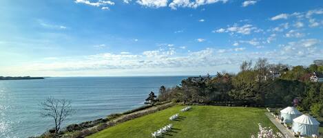 A coastal view with a grassy lawn, white chairs, and yurts by the water.