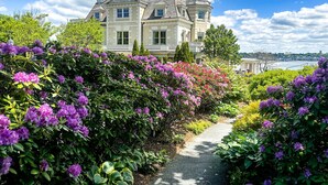 A large, historic house with a prominent balcony, surrounded by lush greenery and vibrant flowers. - The Chanler at Cliff Walk (Newport)