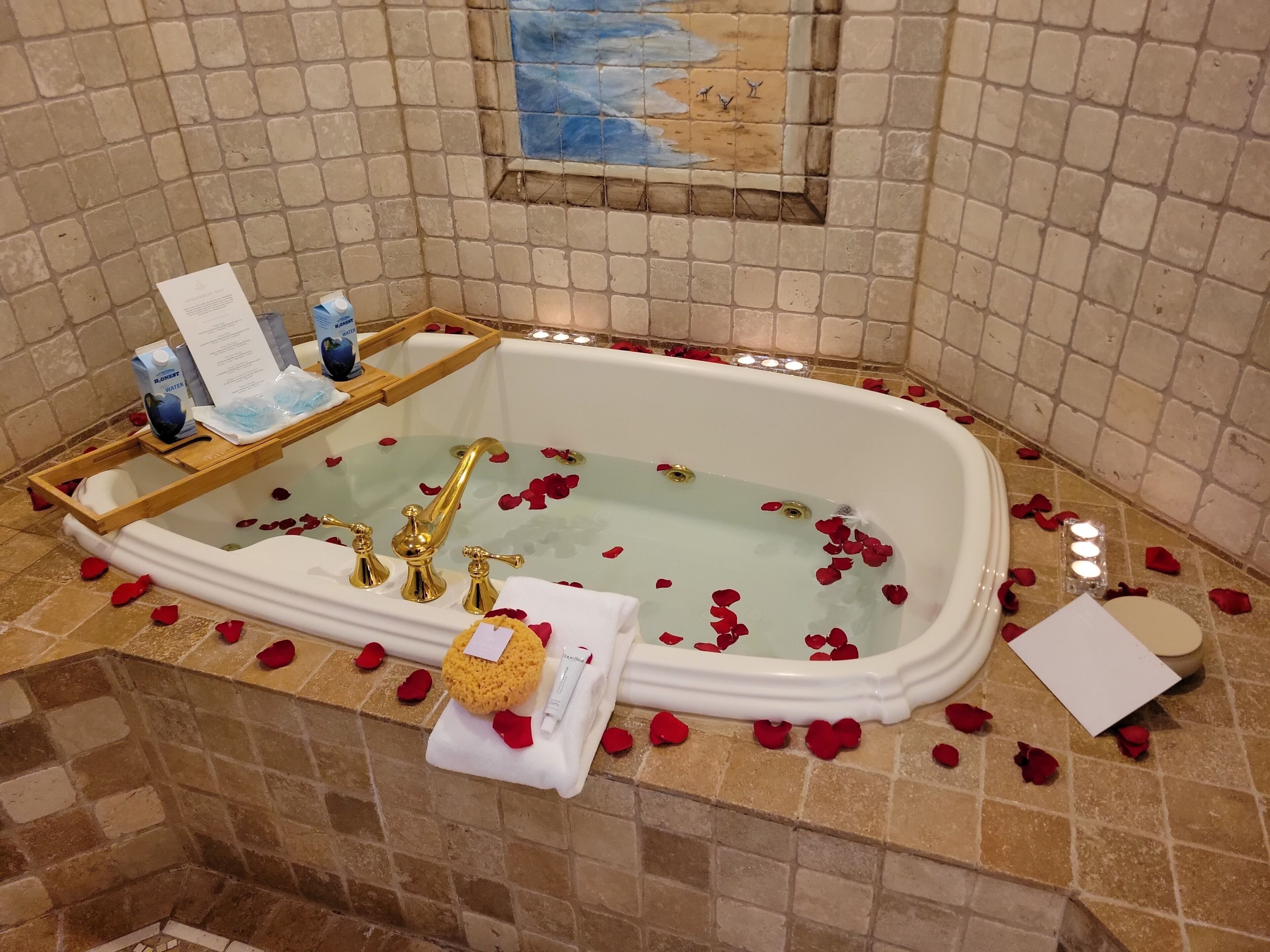 A bathtub with rose petals, a towel, and toiletries.