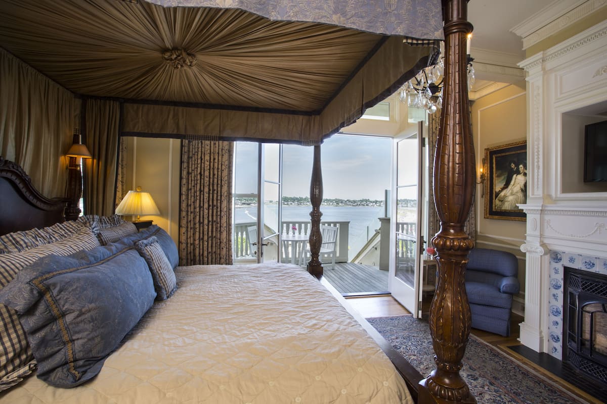 A bedroom with a large bed, a balcony with a view, and a fireplace.