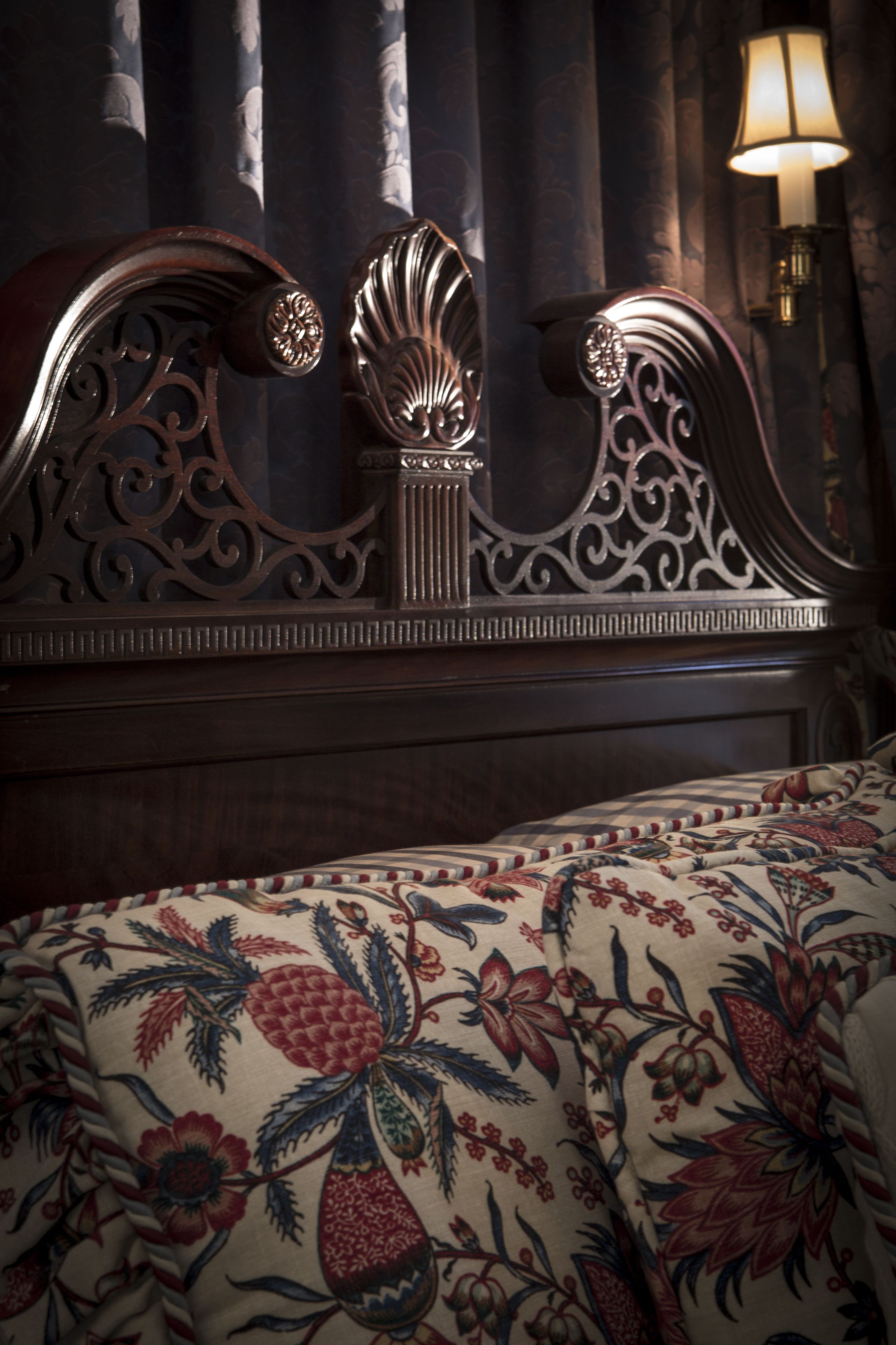 Ein Bett mit blumigem Überwurf und einem verzierten, detailreichen Kopfteil.