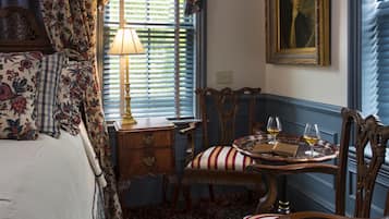 Une chambre à coucher avec un lit, une table de chevet, une lampe, une chaise, une table avec des verres et un tableau accroché au mur.