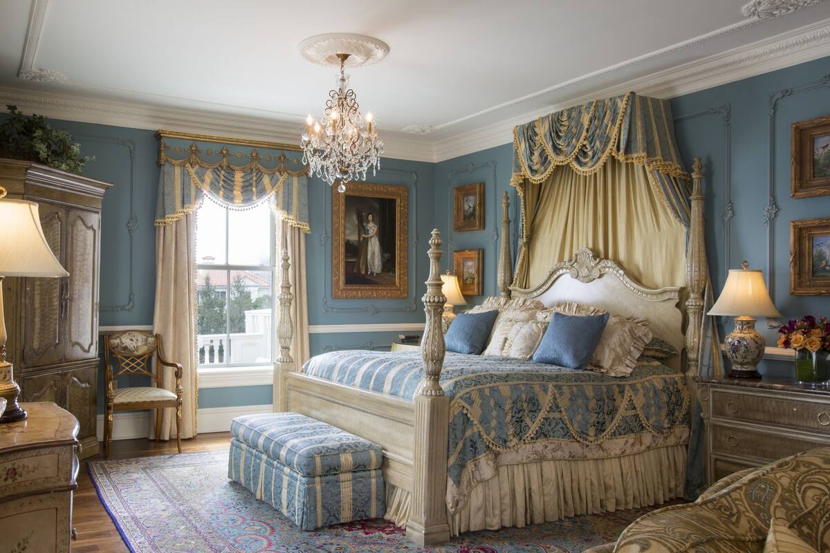 A bedroom with a four-poster bed, ornate curtains, a chandelier, and a large window.