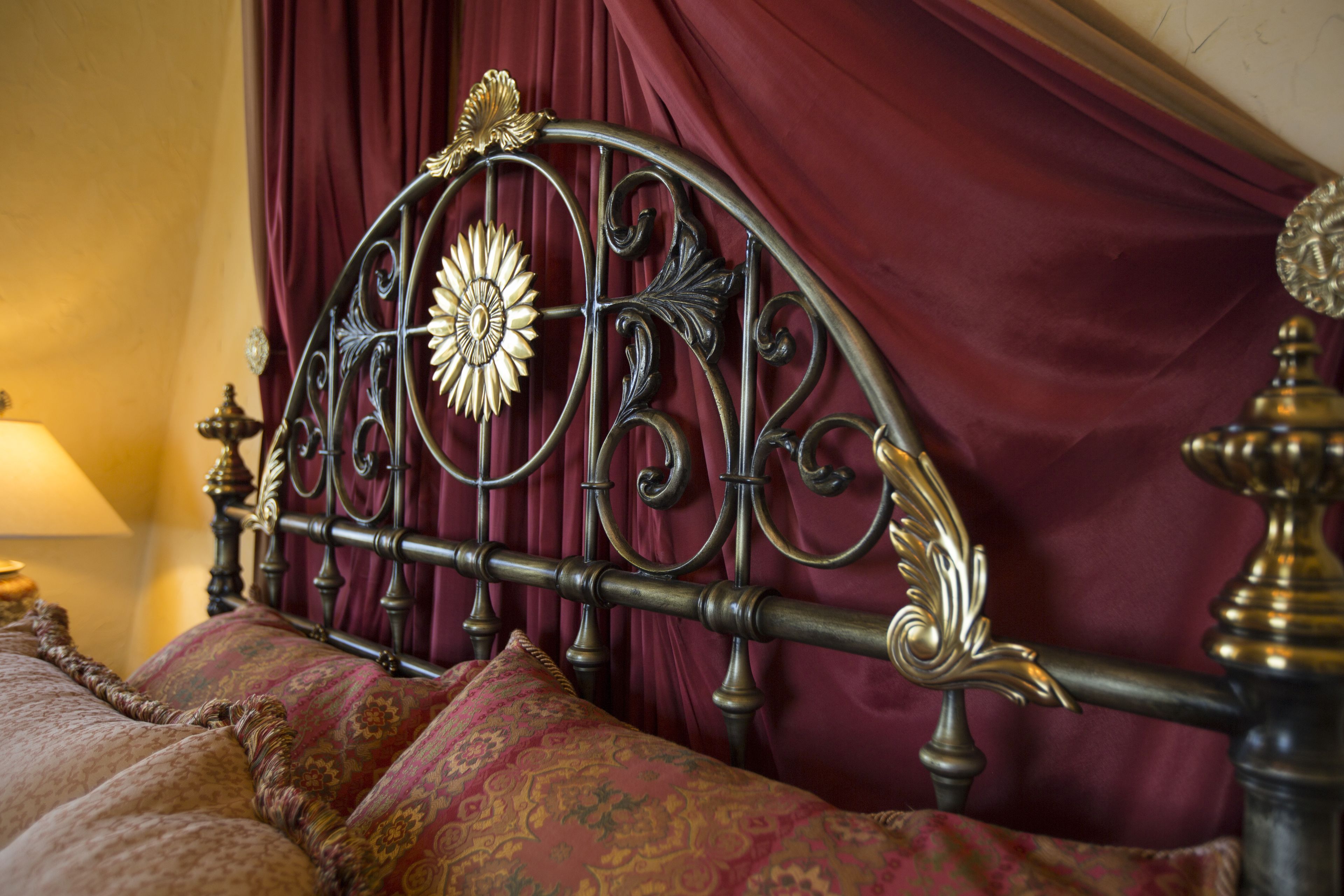 A bed with a decorative metal headboard, a red curtain, and patterned bedding.