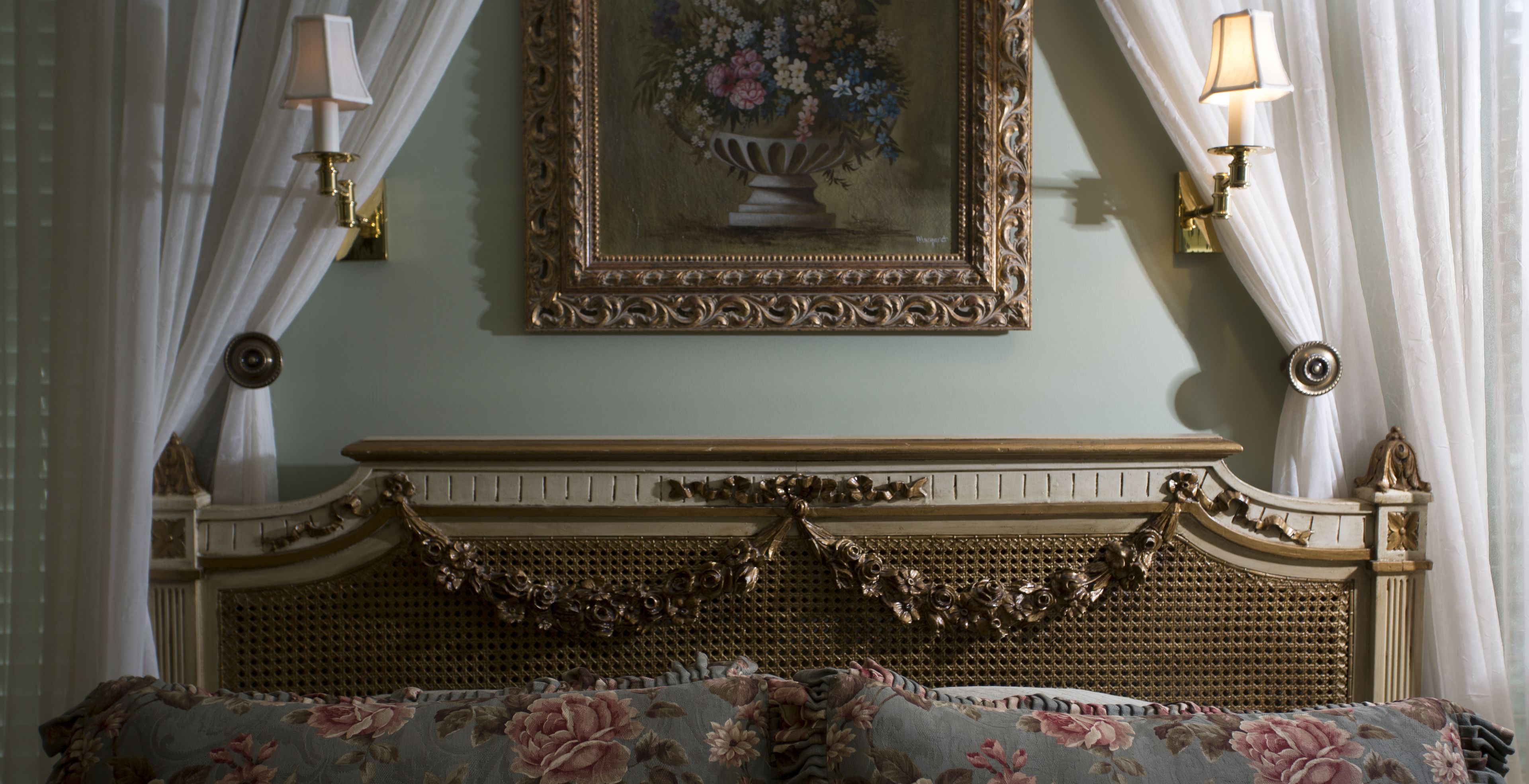 Una cama con cabecera floral, un cuadro de flores enmarcado en la pared y dos apliques.