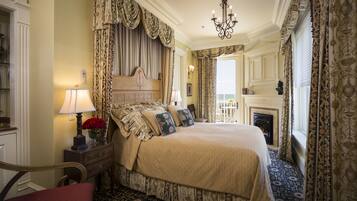 A traditional bedroom with a large bed, ornate curtains, a chandelier, and a fireplace.