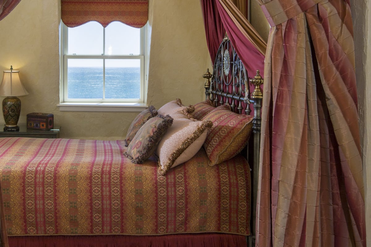 A bedroom with a bed, a window, a lamp, and curtains.