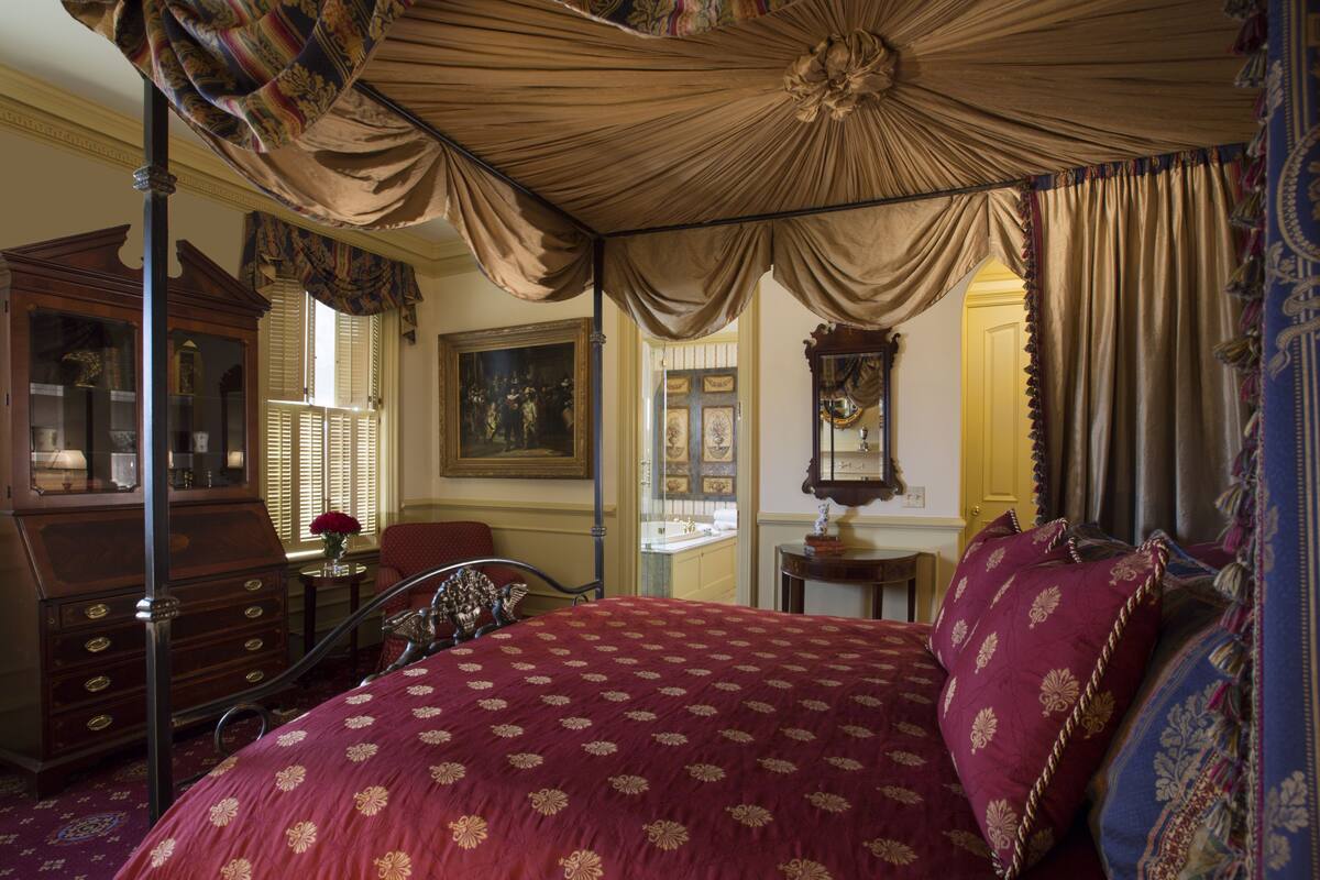 A bedroom with a canopy bed, a wooden dresser, a mirror, and a painting on the wall.