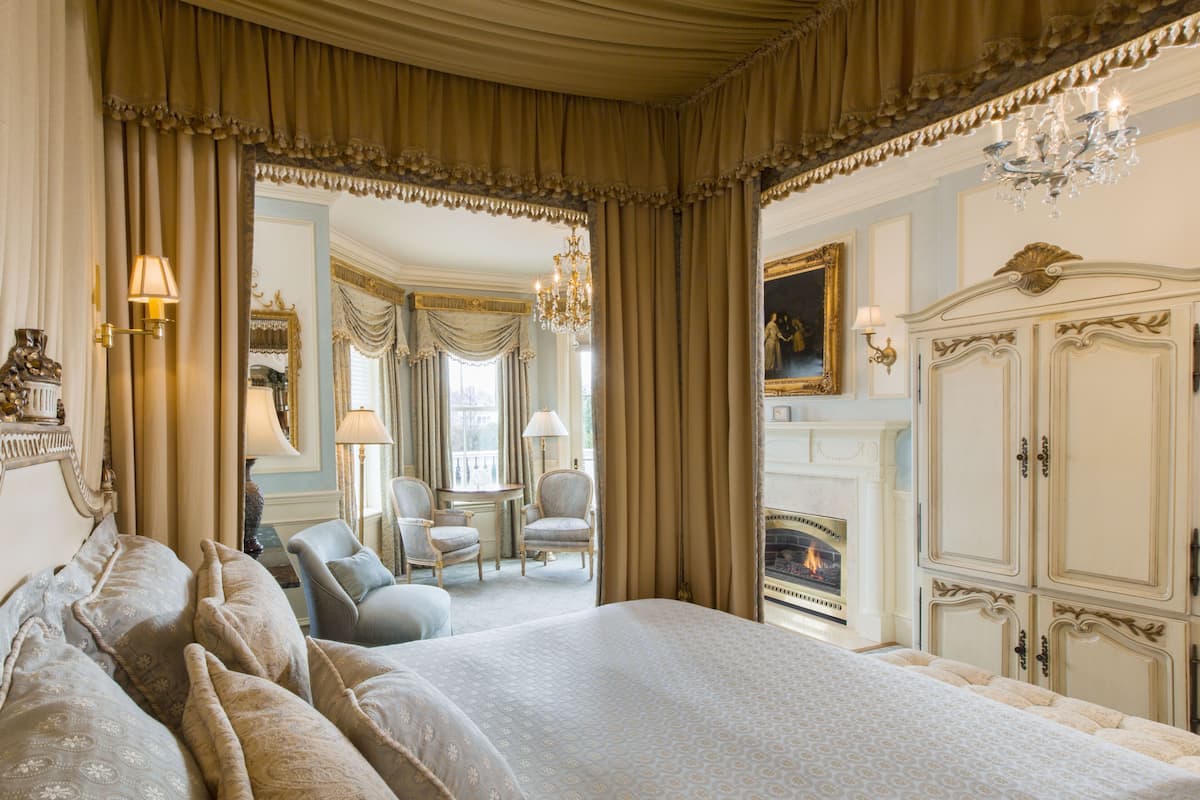 A luxurious bedroom with a large bed, ornate curtains, a chandelier, and a fireplace.