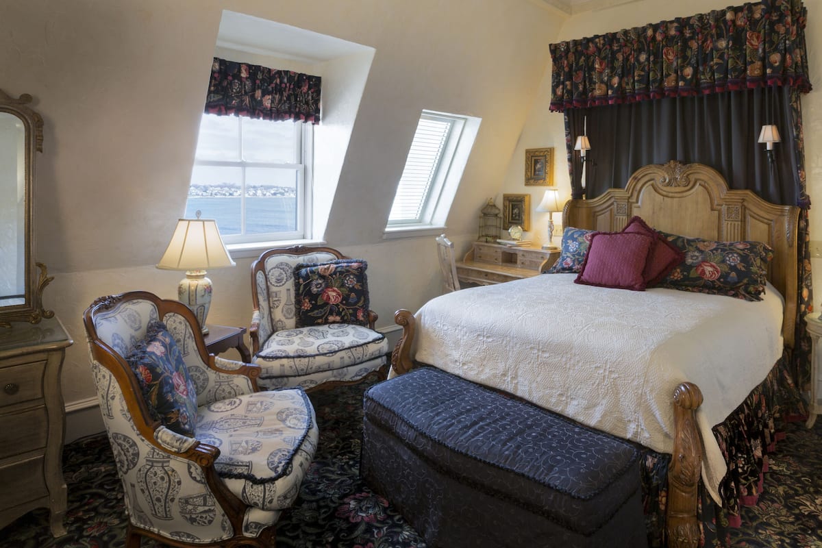 A bedroom with a large bed, a chair, a nightstand, and a window.