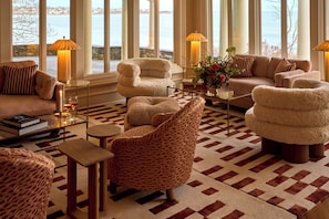 A spacious living room with a view of the water, featuring a sofa, armchairs, a coffee table, and lamps.