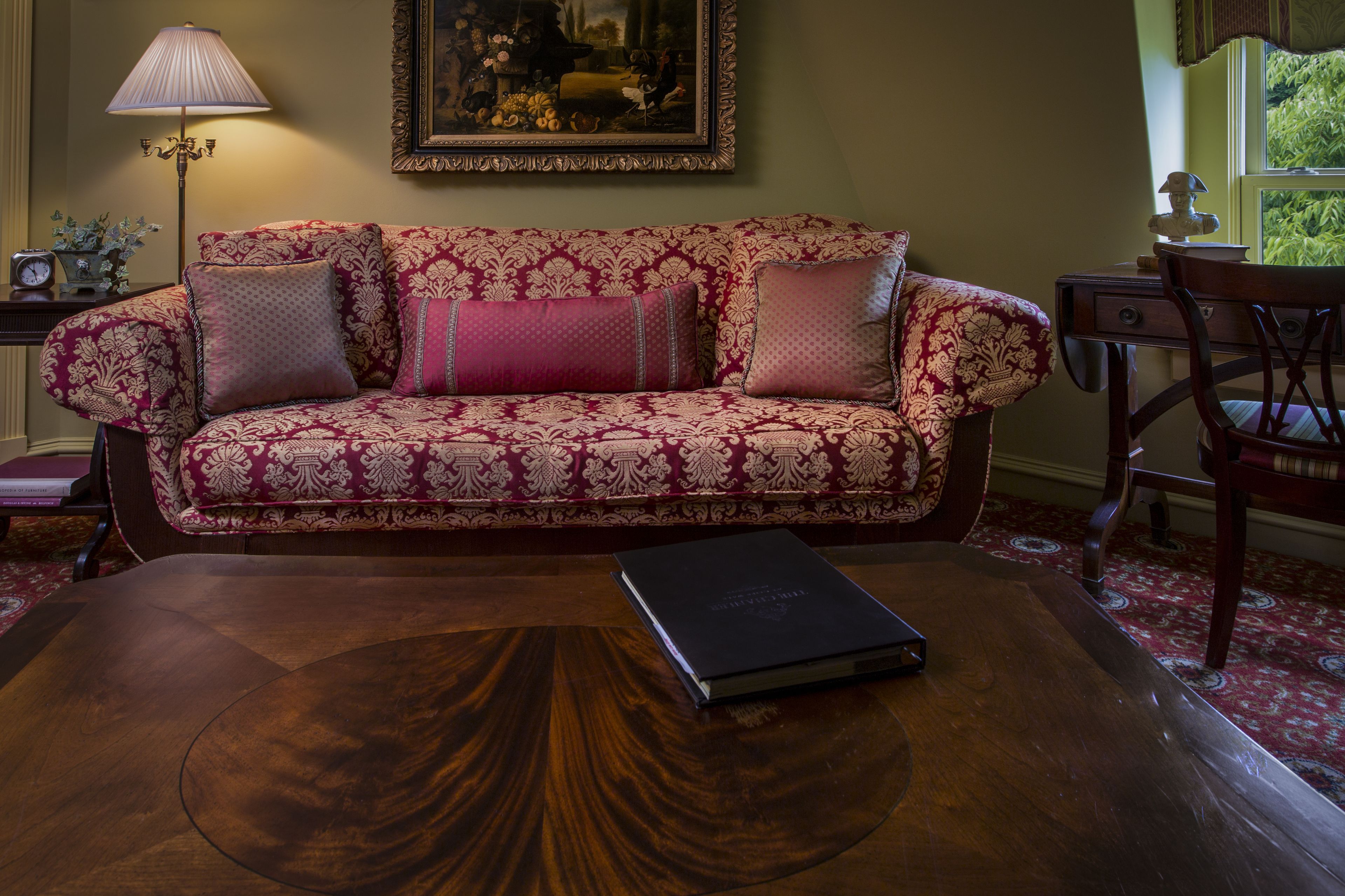 A room with a patterned sofa, a wooden coffee table with a book, a lamp, and a painting on the wall.