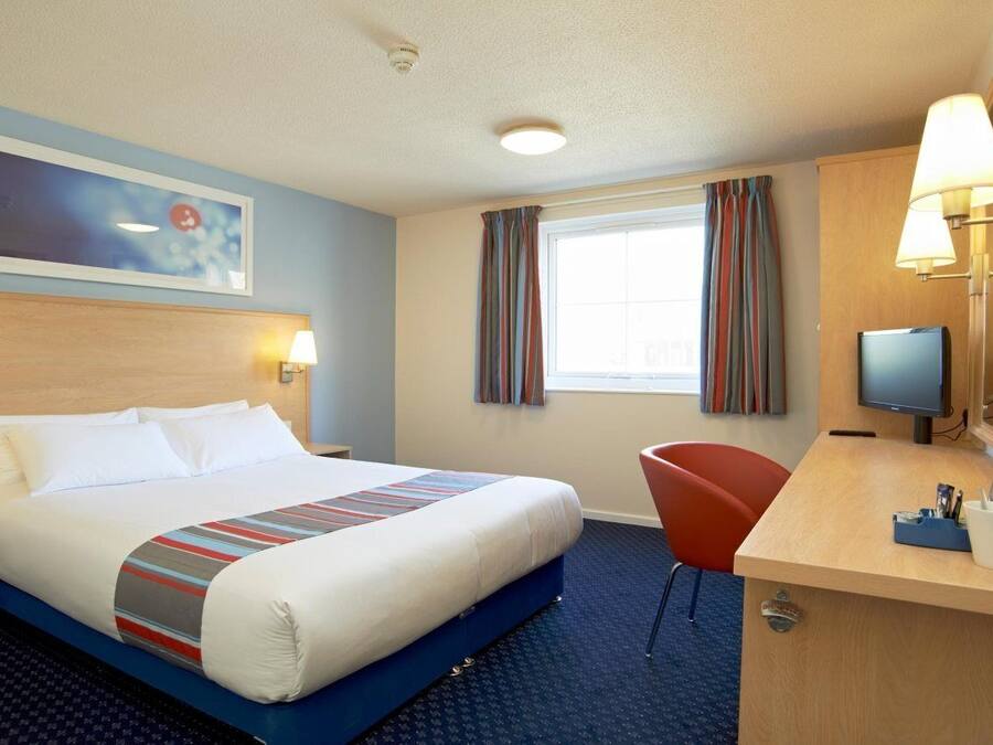 A hotel room with a bed, a desk, a chair, a television, and a window with curtains.