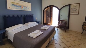 A bedroom with a large bed, a nightstand, a chair, and a painting on the wall. - La Rosa sul Mare (Syracuse)