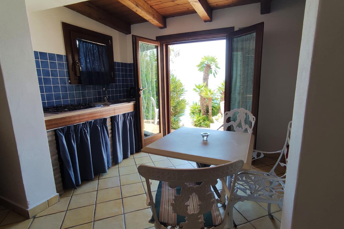 A compact kitchen with a tiled backsplash, wooden ceiling beams, and a sliding glass door leading to a patio with outdoor furniture.