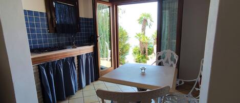 A compact kitchen with a tiled backsplash, wooden ceiling beams, and a sliding glass door leading to a patio with outdoor furniture.