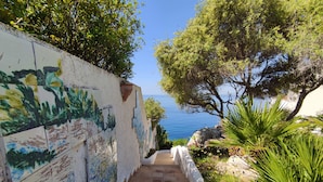 A stone staircase leading to a scenic overlook with a view of the sea, surrounded by lush greenery and a tiled wall with colorful artwork. - La Rosa sul Mare (Syracuse)