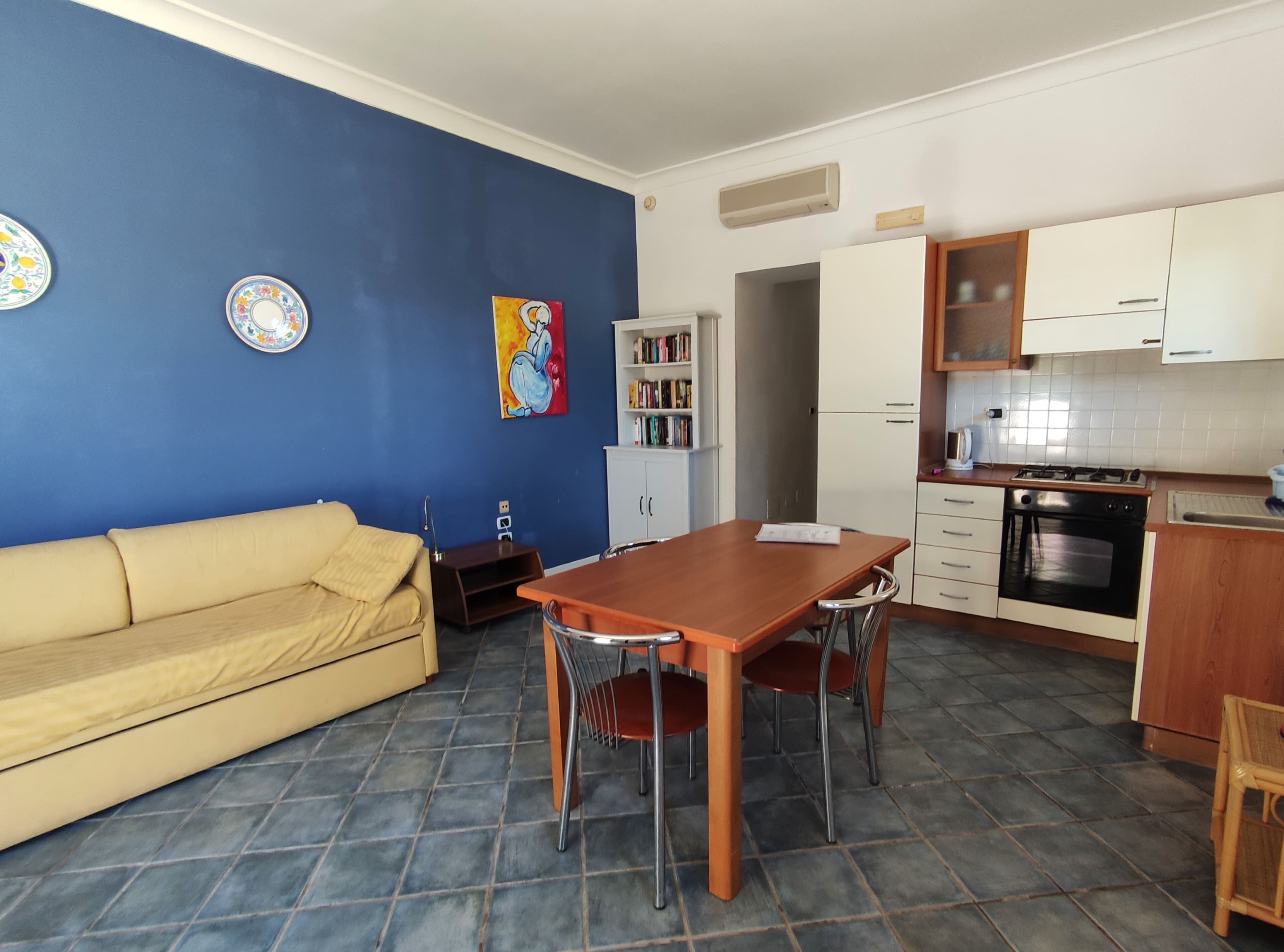 Een ruimtelijk ingerichte leefruimte met een eethoek, kitchenette en een slaapbank.
