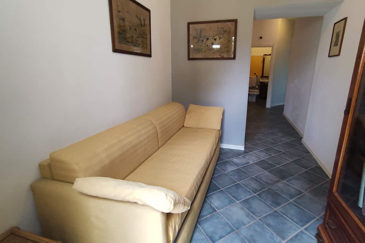A room with a beige sofa, two framed pictures on the wall, and a tiled floor.