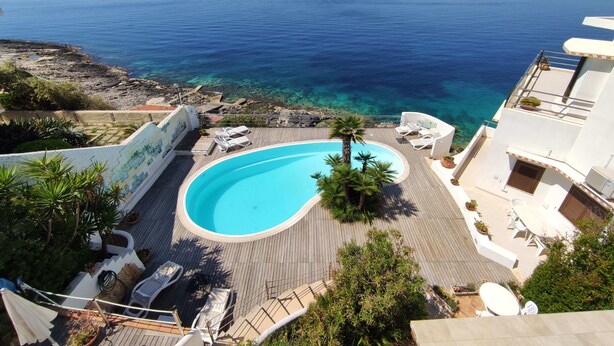 A pool with a view of the sea, surrounded by lounge chairs and a wooden deck. - La Rosa sul Mare (Syracuse)