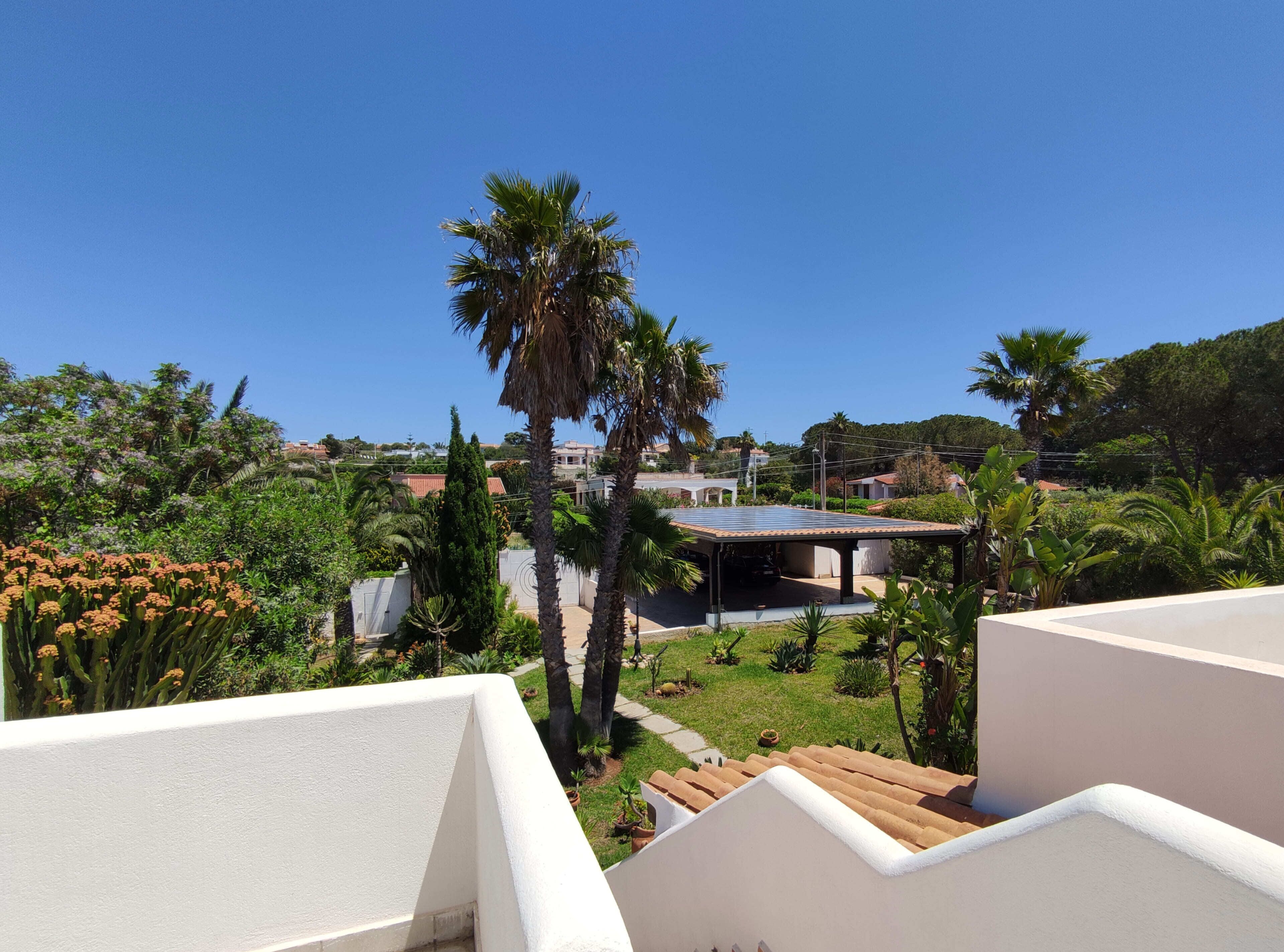 A rooftop terrace with a view of a garden, a covered outdoor area, and a building in the background.
