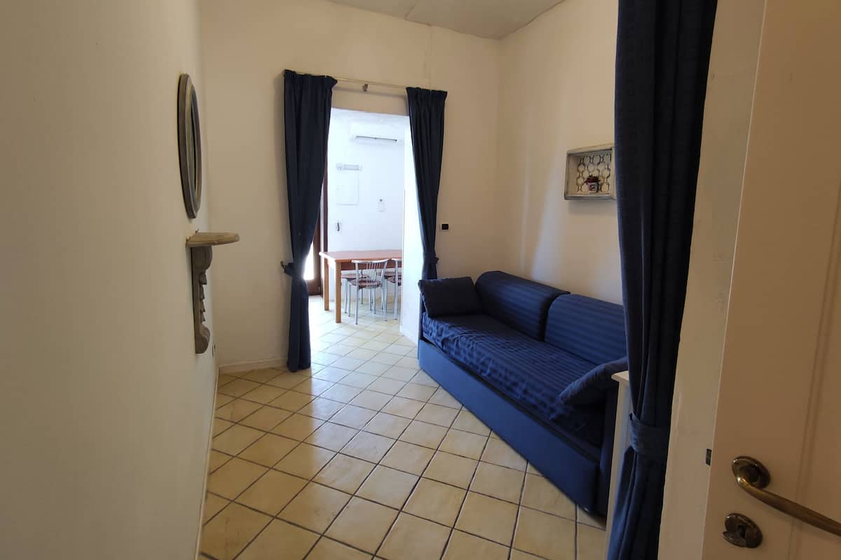 A room with a sofa, a dining table with chairs, and a tiled floor.