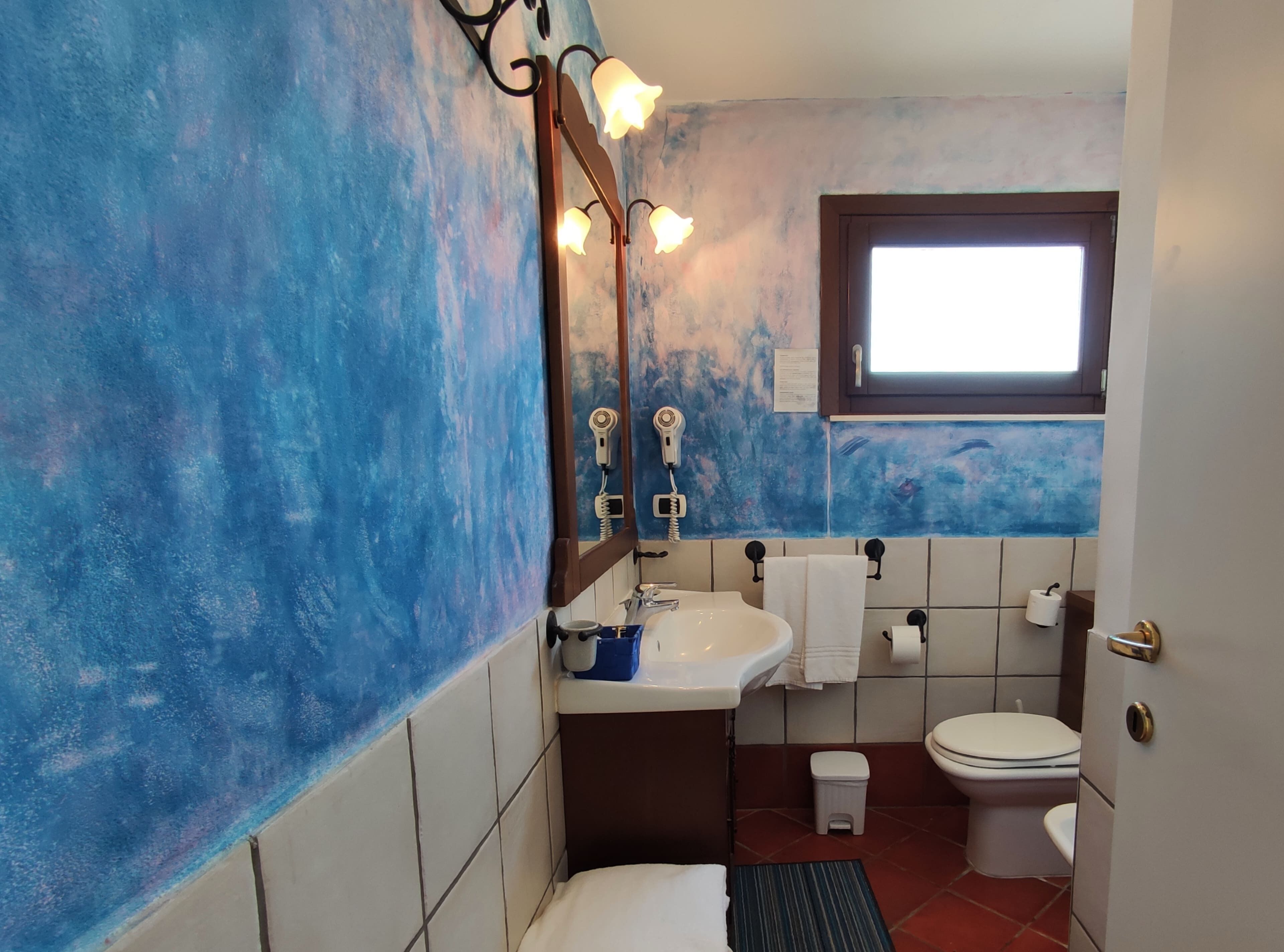 A bathroom with a blue textured wall, a sink, a toilet, and a window.